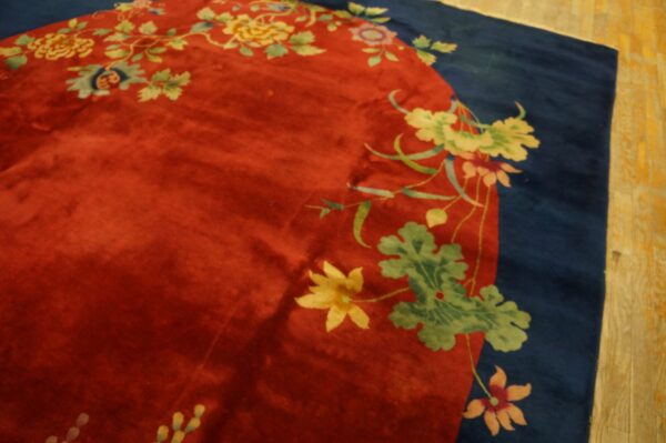 Close-up of a red, lustrous rug with a navy border and vibrant yellow and green floral vine patterns.