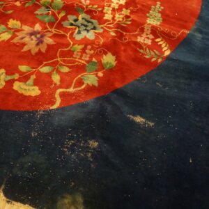 High-pile red rug with yellow and green florals next to a worn navy section on wood flooring.