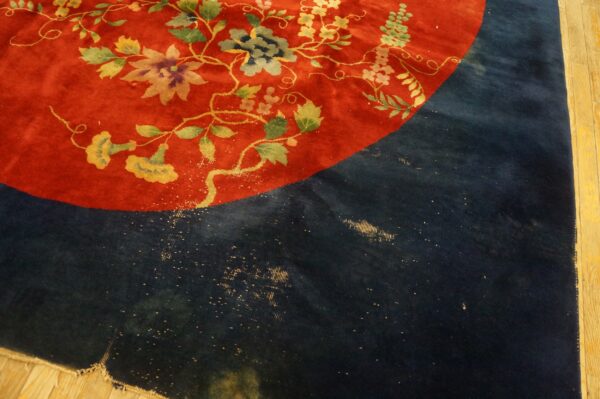 High-pile red rug with yellow and green florals next to a worn navy section on wood flooring.