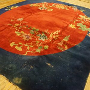 Rust-red and navy rug featuring a central floral wreath motif lying on blonde hardwood planks.