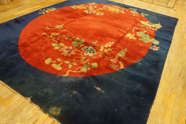 Rust-red and navy rug featuring a central floral wreath motif lying on blonde hardwood planks.