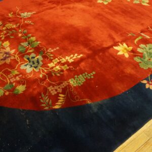 Ornate floral vines decorate a plush red central field bordered by dark blue on wood flooring.