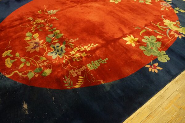 Ornate floral vines decorate a plush red central field bordered by dark blue on wood flooring.