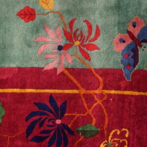 A teal and red rug features a floral and butterfly design next to a wooden plank floor.