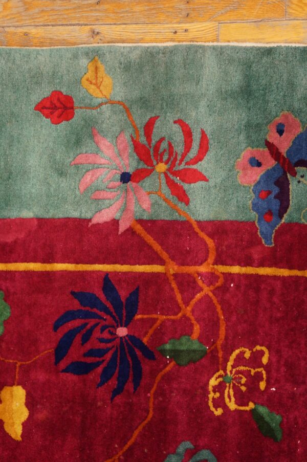A teal and red rug features a floral and butterfly design next to a wooden plank floor.