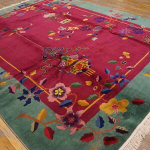 Multi-colored floral rug featuring a magenta field and teal border laid on aged wood floors.