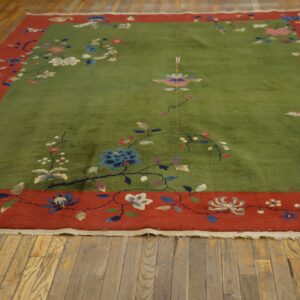 Sage green area rug with an elaborate multicolored floral design and a wide brick red border on wood floors.