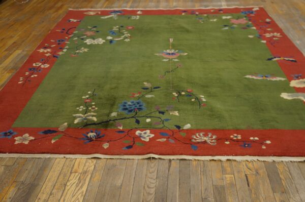 Sage green area rug with an elaborate multicolored floral design and a wide brick red border on wood floors.