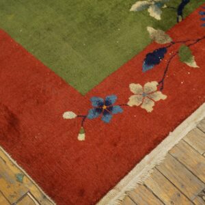 Green and rust floral rug corner featuring blue and cream flowers on distressed wood planks.