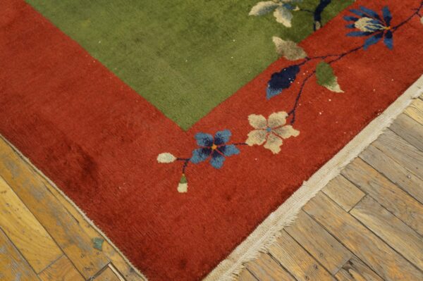 Green and rust floral rug corner featuring blue and cream flowers on distressed wood planks.
