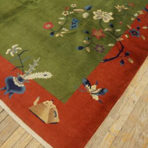 Plush green floral rug with a rust border featuring vases and a butterfly lies on worn wood floors.