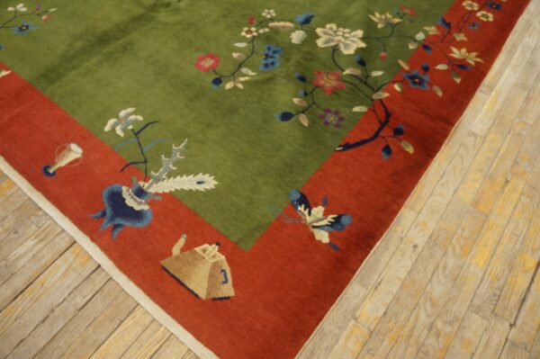 Plush green floral rug with a rust border featuring vases and a butterfly lies on worn wood floors.