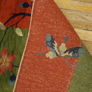 A red and green floral pile rug is folded, exposing a flat woven backing with a butterfly design.
