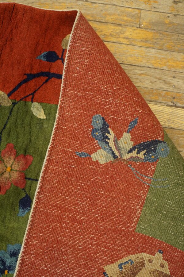 A red and green floral pile rug is folded, exposing a flat woven backing with a butterfly design.