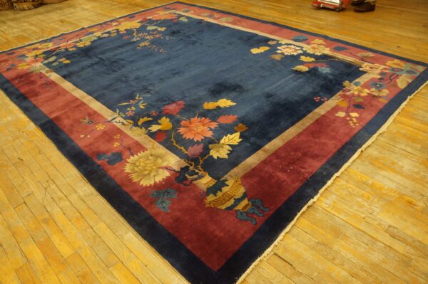 Navy blue area rug with maroon and tan borders features a detailed floral vine pattern on wood flooring.