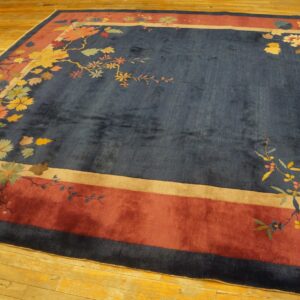 Navy rug features multicolor floral branches, a wide rust-red border, and a plush pile on wood flooring.