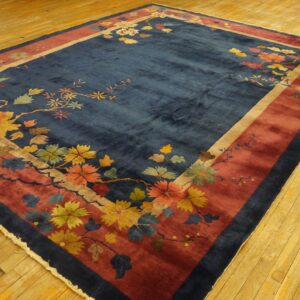 Navy blue rug with multicolored autumn floral motifs and a wide red border on yellow wooden floorboards.