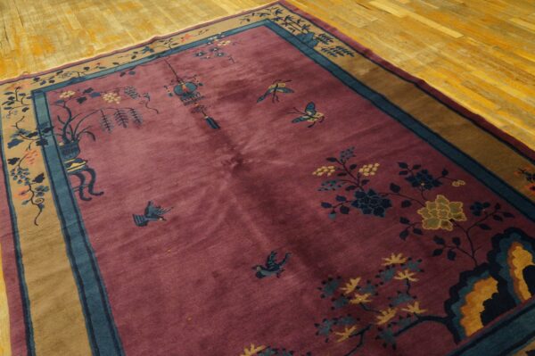 Maroon rug with blue and yellow floral and butterfly motifs and tan border on a shiny wood plank floor.