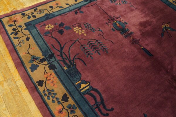 Plush maroon rug with a camel floral border and teal accents rests on light wood flooring.
