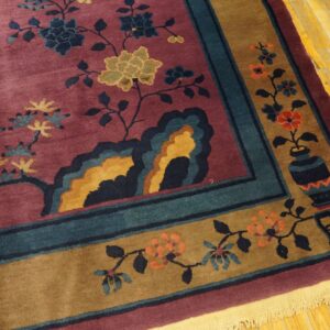 Low-pile burgundy rug featuring floral designs and a patterned border, set on distressed yellow wood floors.