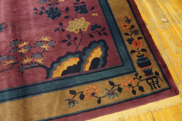 Low-pile burgundy rug featuring floral designs and a patterned border, set on distressed yellow wood floors.