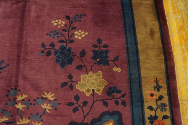 Deep mauve rug with stylized navy and mustard floral vines next to a wide tan and teal striped border.