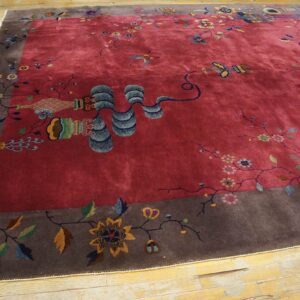 Plush berry-red rug with a wide gray-brown border, multicolored floral and object patterns, resting on wood.