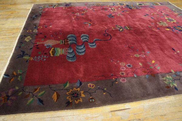 Plush berry-red rug with a wide gray-brown border, multicolored floral and object patterns, resting on wood.