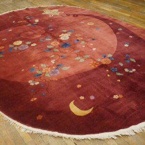 Round red rug with a swirling field pattern, multicolored florals, a crescent moon, and white fringe on wood.