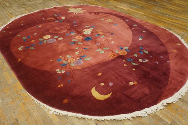 Round red rug with a swirling field pattern, multicolored florals, a crescent moon, and white fringe on wood.