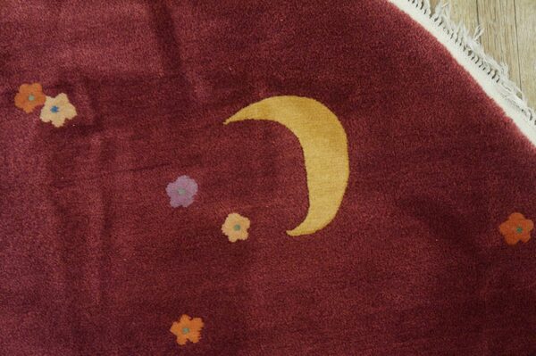Plush burgundy rug featuring a golden crescent moon and scattered small flowers on light wood flooring.