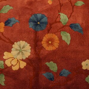 Close-up of a low-pile rug featuring a rust-red background with colorful floral vine patterns.