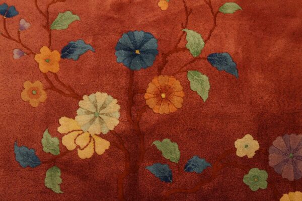 Close-up of a low-pile rug featuring a rust-red background with colorful floral vine patterns.