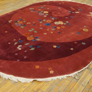 Burgundy oval rug displaying multicolored flowers and a spiral design on distressed hardwood flooring.