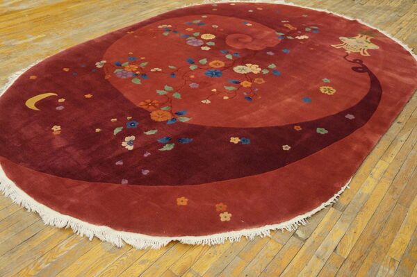Burgundy oval rug displaying multicolored flowers and a spiral design on distressed hardwood flooring.