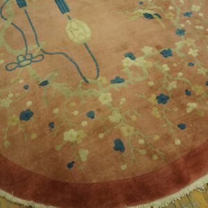 Round salmon-colored rug featuring a teal and pale green floral vine pattern with a rust border on wood floors.