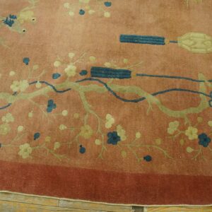 Round reddish-pink rug with sage green floral vines and teal decorative motifs on wood flooring.