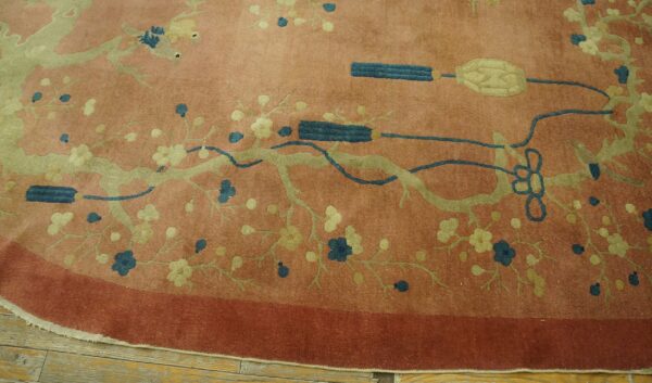 Round reddish-pink rug with sage green floral vines and teal decorative motifs on wood flooring.