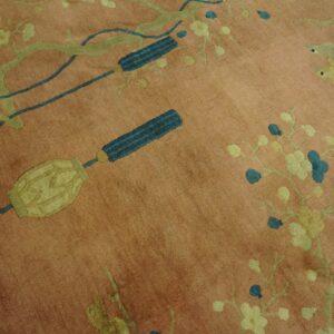 Salmon pink rug detailed with green branches, teal blossoms, yellow birds, and decorative blue tassels.