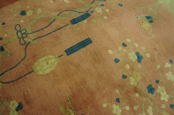 Salmon pink rug detailed with green branches, teal blossoms, yellow birds, and decorative blue tassels.