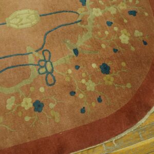 Dusty rose rounded rug corner featuring blue and green floral patterns on worn wood planks.