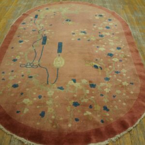 Oval dusty rose rug with blue and cream floral pattern, resting on worn wooden floorboards.
