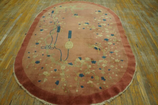 Oval dusty rose rug with blue and cream floral pattern, resting on worn wooden floorboards.