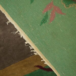 Flatweave rug featuring green and red floral patterns rests upon a dark brown and green pile rug.