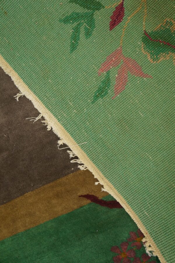 Flatweave rug featuring green and red floral patterns rests upon a dark brown and green pile rug.