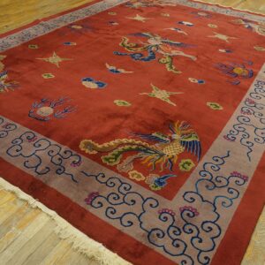 Rectangular red rug with multicolored phoenix pattern, a wide grayish-mauve border, and fringe on wood planks.