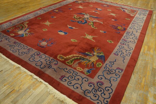 Rectangular red rug with multicolored phoenix pattern, a wide grayish-mauve border, and fringe on wood planks.