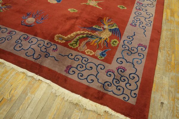 Rust-colored rug featuring a detailed colorful bird and scroll border lying on distressed wood planks.