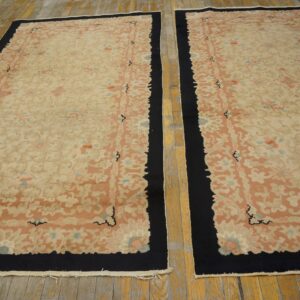 Matching floral rugs in pink and beige with black borders are laid on a distressed wood floor.