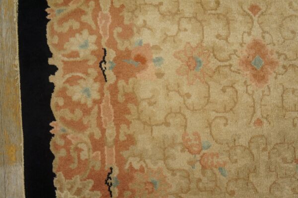 Tan rug detail showing peach floral motifs, teal accents, a black border, and weathered wood flooring.
